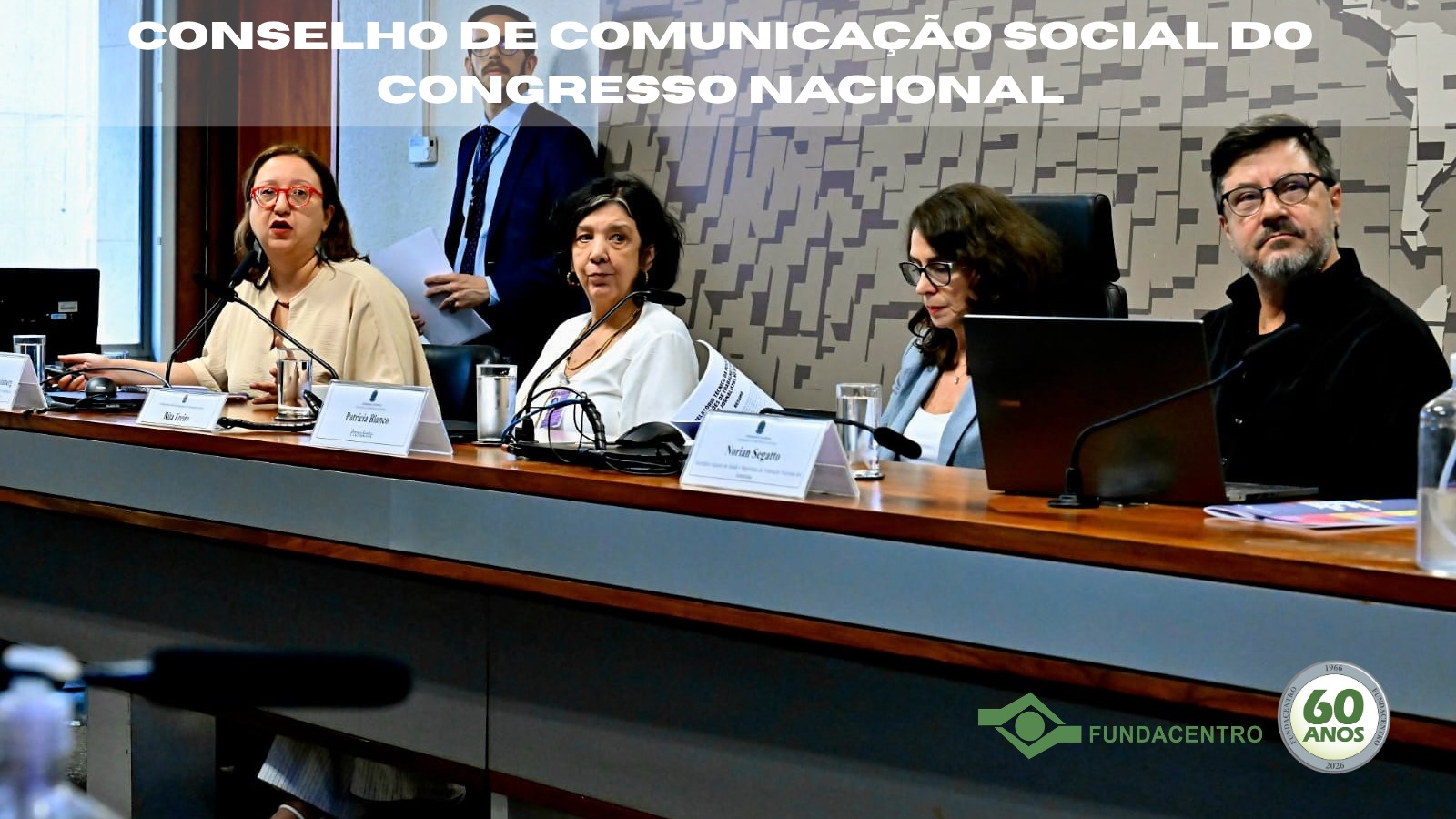 Para Todos Verem: Mesa com Cristiane Reimberg, Rita Freire, Patrícia Blanco e Norian Segatto. No topo, Conselho de Comunicação Social do Congresso Nacional. No canto inferior direito, a marca da Fundacentro com selo dos 60 anos. Foto: Waldemir Barreto/Agência Senado.