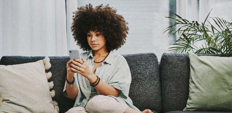 Mulher, sentada em um sofá, usa um telefone celular