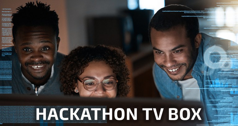 A imagem mostra três pessoas sorrindo, olhando atentamente para uma tela de computador. Elas estão envolvidas em um ambiente de trabalho colaborativo, típico de um hackathon. Além de códigos de informática, na imagem aparece o letreiro "Hackathon TV Box".