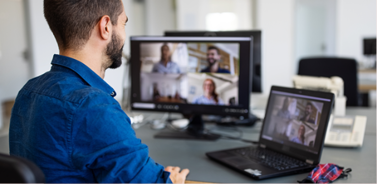 Foto de homem em frente a notebook e tela, acompanhando reunião virtual