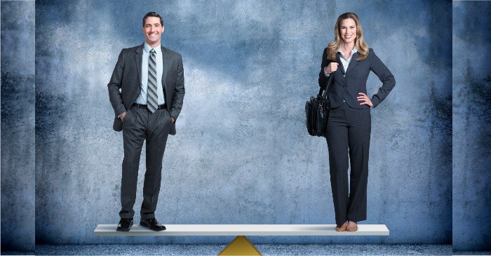 Um homem e uma mulher estão em equilíbrio sobre uma estrutura similar a uma balança, uma plataforma com um único ponto de apoio. Uma metáfora visual da Equidade de Gênero.