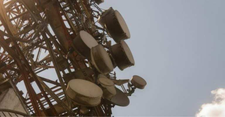 A imagem mostra uma estrutura metálica de telecomunicações, provavelmente uma torre de transmissão. Nela, são visíveis várias antenas parabólicas de diferentes tamanhos, que parecem estar orientadas em diferentes direções.