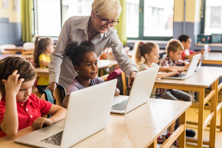 Estudantes orientados por uma professora utilizam laptops em uma sala de aula.