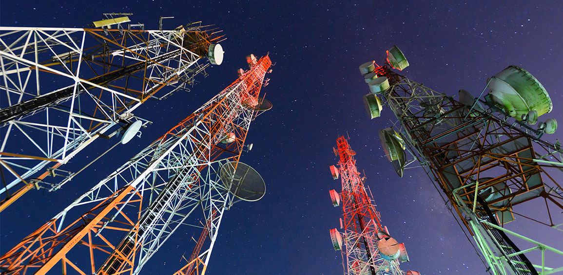 Quatro torres coloridas sustentam antenas para serviços de telecomunicações, como telefonia móvel. As estruturas sob um céu noturno e estrelado mesclam cores como o branco, o laranja, o vermelho e o verde.