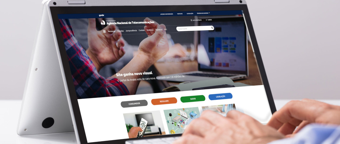 Novo portal da Anatel sendo mostrado na tela de um notebook com mãos de homem próximas do teclado
