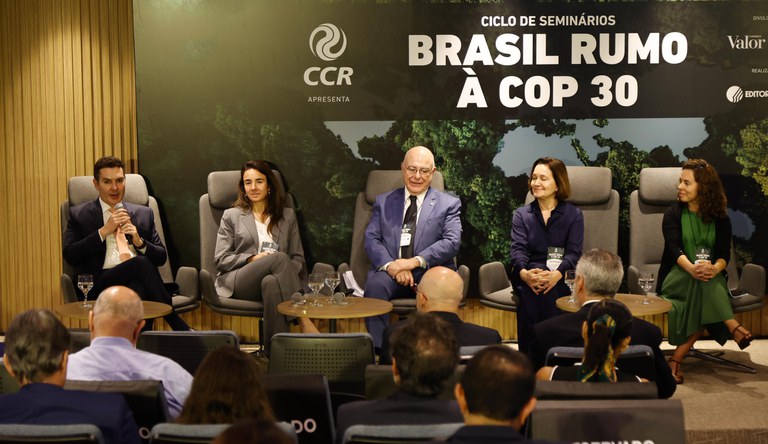 Na foto o ministro Jader Filho ao microfone ao lado de outras autoridades sentados a frente de um painel com os dizeres "Ciclo de Seminários Brasil Rumo a COP 30"