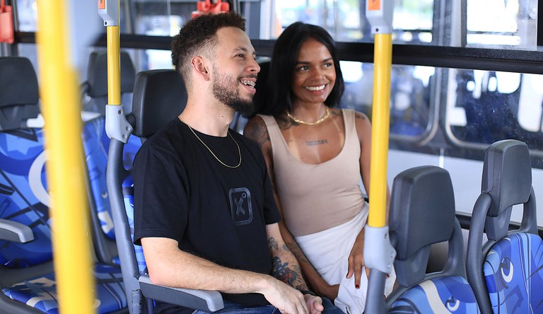 Na capa casal de passageiros sentados dentro de um ônibus