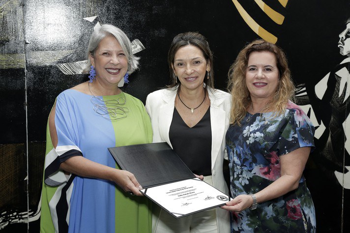 Dalila Oliveira (centro) recebe o diploma das mãos da diretora da FaE, Andrea Moreno, e da reitora Sandra GoulartFoto Foca Lisboa | UFMG