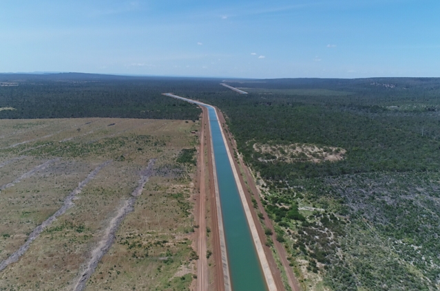 Vista aérea de canal com água atravessando área de vegetação e terreno aberto