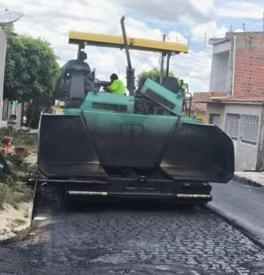 Máquina aplica asfalto sobre rua pavimentada com paralelepípedos.