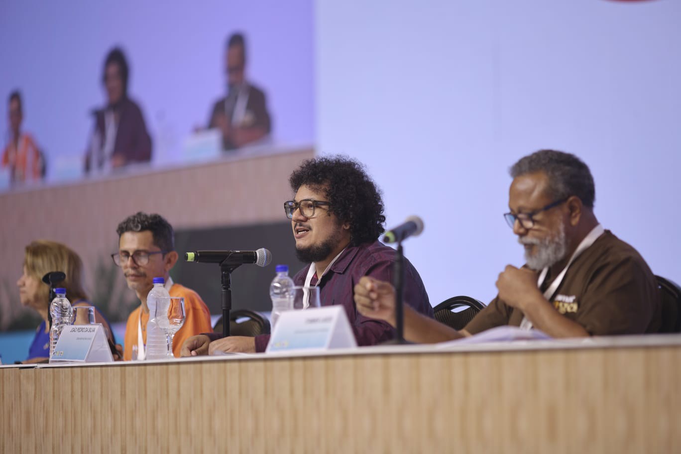 Foto: Thiago Lustosa Fotografia - participantes da mesa do eixo 3: Itamar Lages (UPE), João Pedro (CNS), Itamar Lages (UPE), Cledson Sampaio (CNS) e Francisca Valda (CNS).  Eles estão sentados à mesa do auditório. 