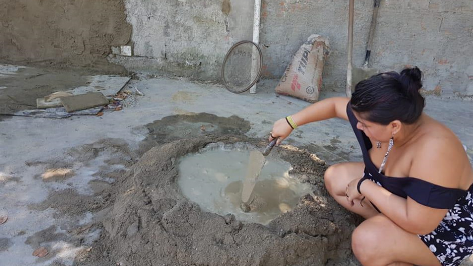 Uma pessoa indígena preparando cimento para rebocar o muro que será pintado