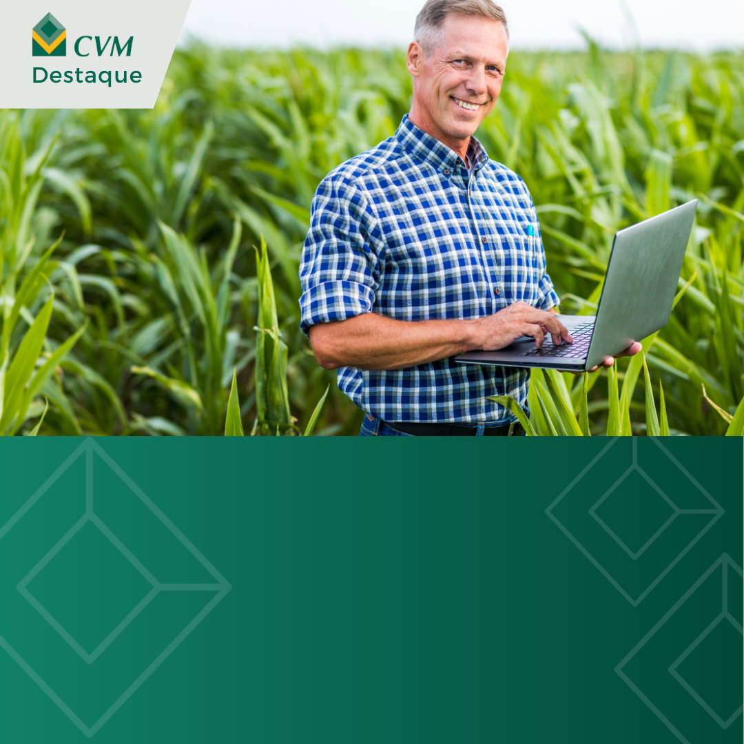 com imagem de homem de meia-idade, com cabelos grisalhos, sorrindo e segurando laptop em campo de cultivo verde. Ele veste camisa xadrez azul e calça jeans. No canto superior esquerdo, logo "CVM Destaque". A parte inferior da imagem é preenchida com uma cor verde sólida, sobre a qual está o logotipo de CVM repetido em um padrão suave. A imagem parece ser destinada a destacar notícias ou informações relacionadas ao setor agrícola.