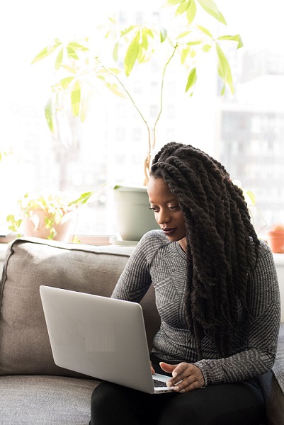 Imagem de uma mulher sentada em um sofá cinza, utilizando um laptop. Link para o acesso ao Cadastur.