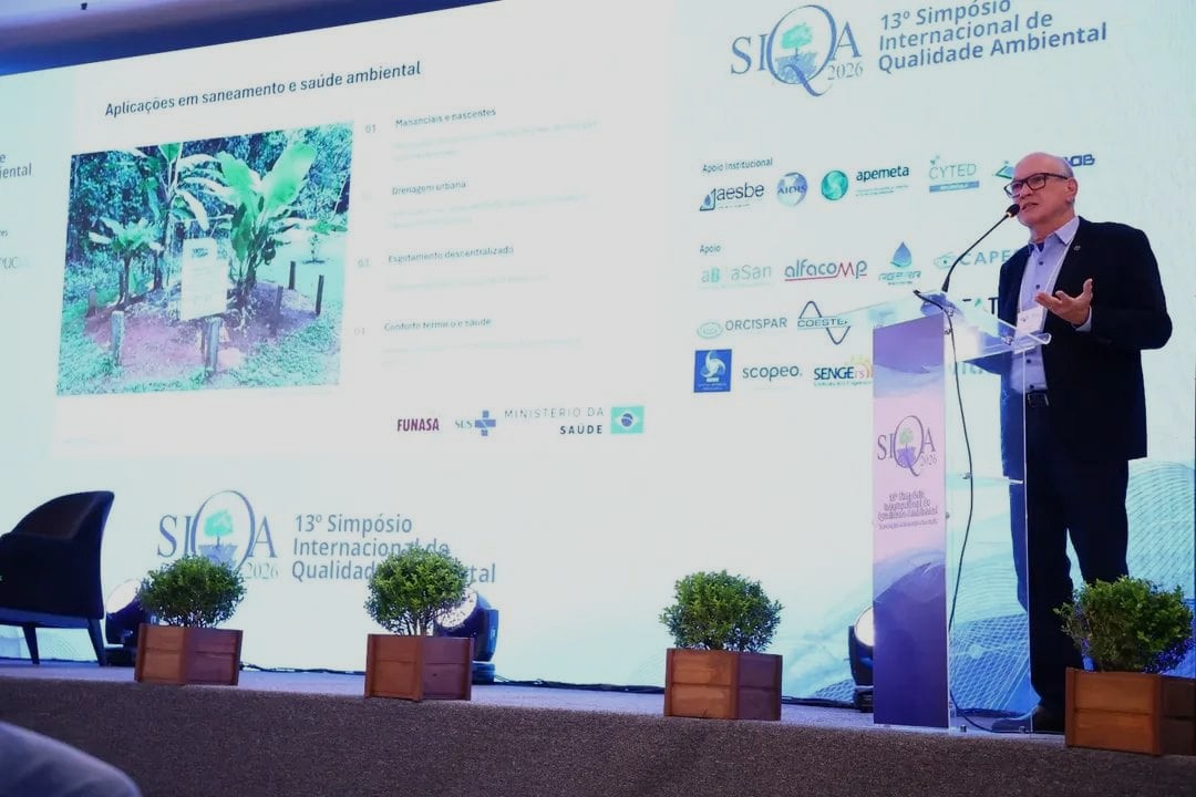 Homem discursa em púlpito no palco durante o 13º Simpósio Internacional de Qualidade Ambiental.