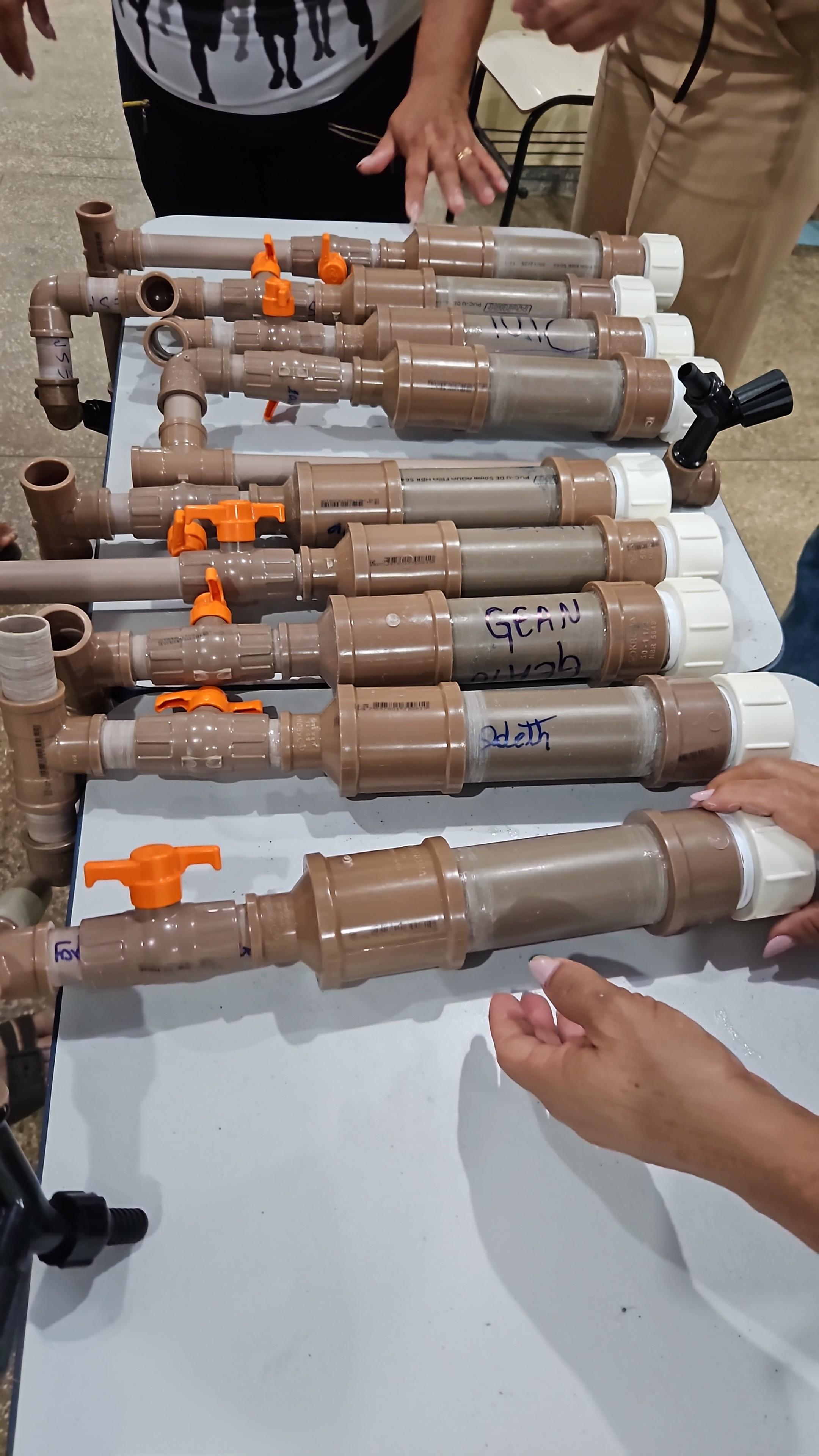 Dosadores de cloro artesanais feitos com tubos de PVC marrom alinhados sobre uma mesa cinza clara.