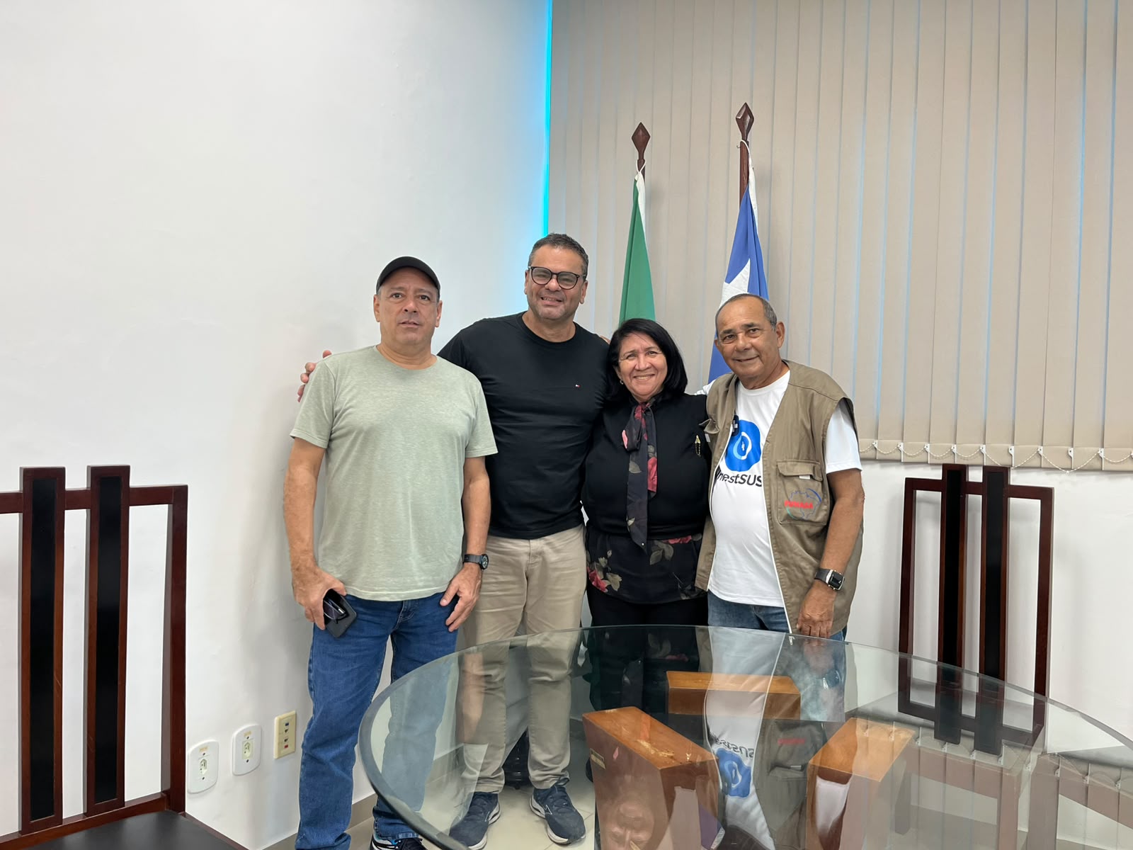Quatro pessoas, 3 homens e uma mulher posam para foto em escritório municipal.