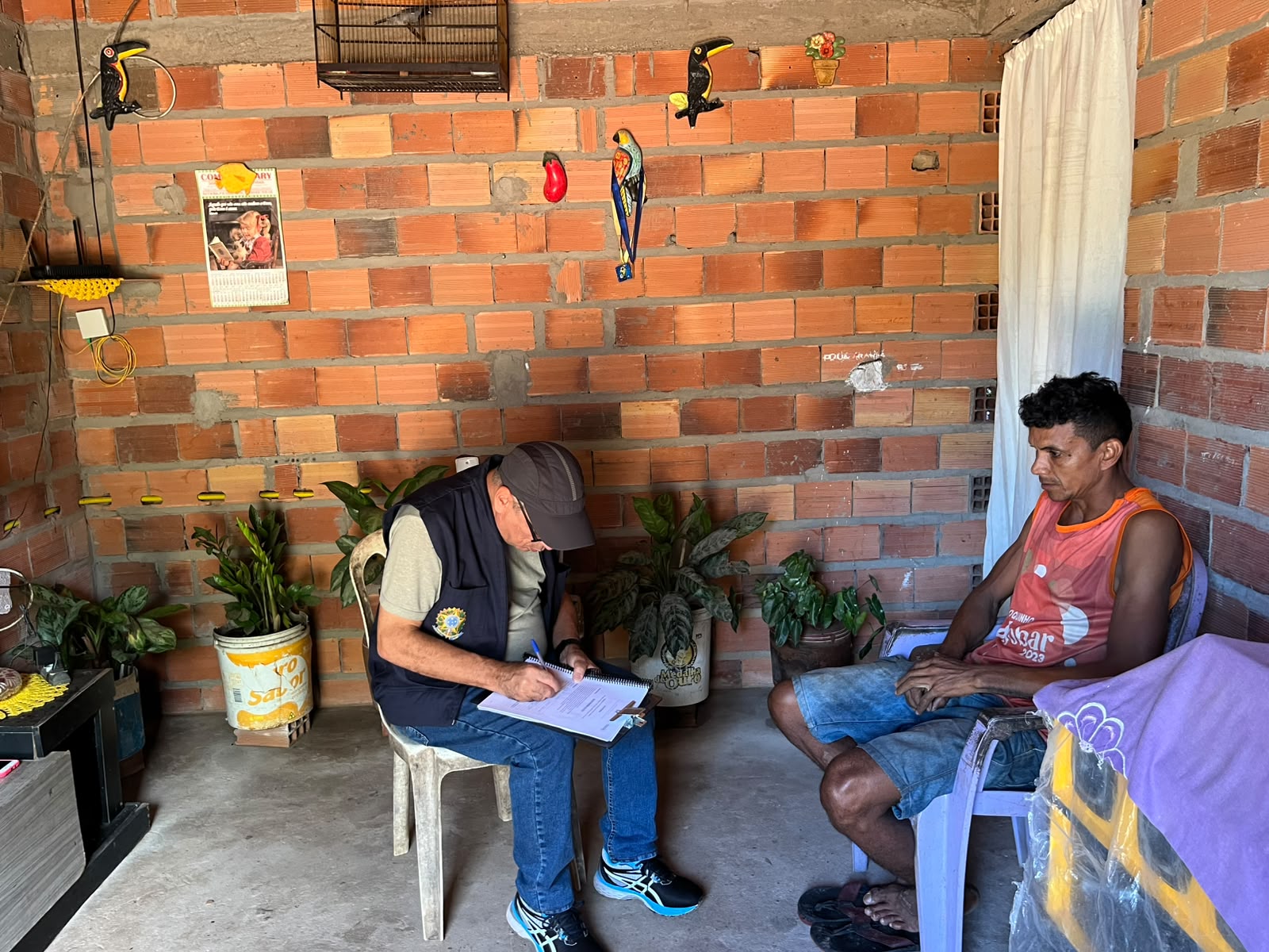 Dois homens sentados de frente um para o outro, um deles de colete, recolhe a sugestão do morador.