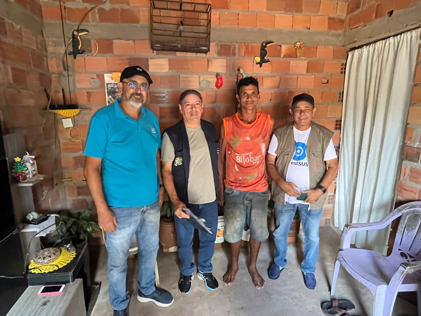 Quatro homens posando para foto em casa de paredes rusticas.