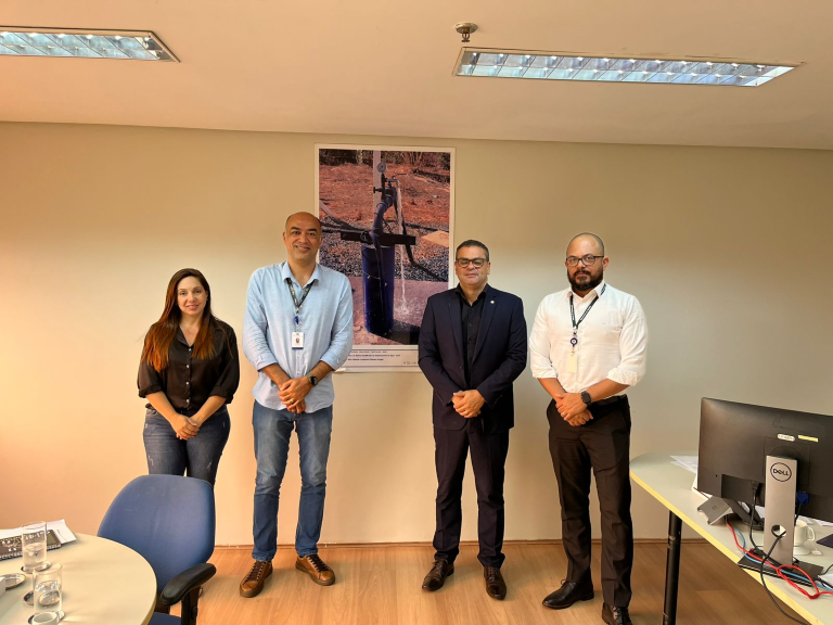 Três homens e uma mulher posando para uma foto ao fundo de uma parede branca com um poster do Salta-Z.
