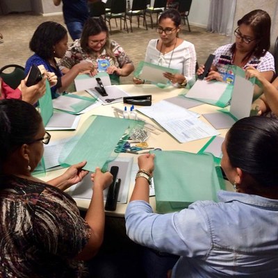 Mulheres trabalham com pastas em volta de uma mesa redonda