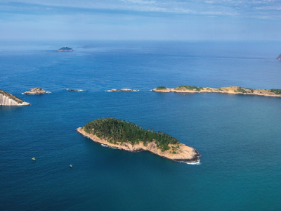 Foto com seis ilhas que compõem o Monumento Natural das Ilhas Cagarras no mar aberto. Ilha Rasa ao fundo no lado superior esquerdo.