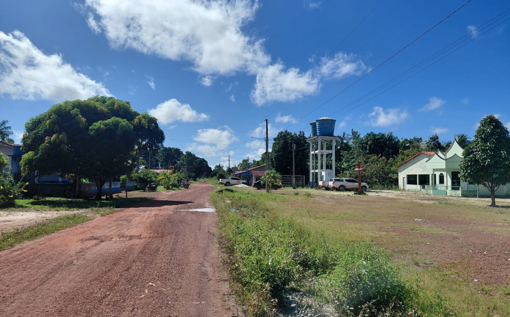 Rua de terra inserida no assentamento, com construções nas laterais