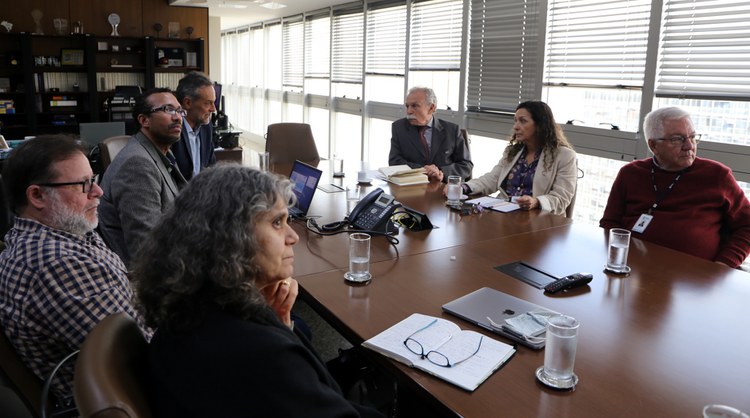 Imagem com representantes do Instituto Nacional de Tecnologia da Informação (ITI) e do CNPQ sentados ao redor de uma mesa grande, marrom, assistindo a uma apresentação durante a reunião.