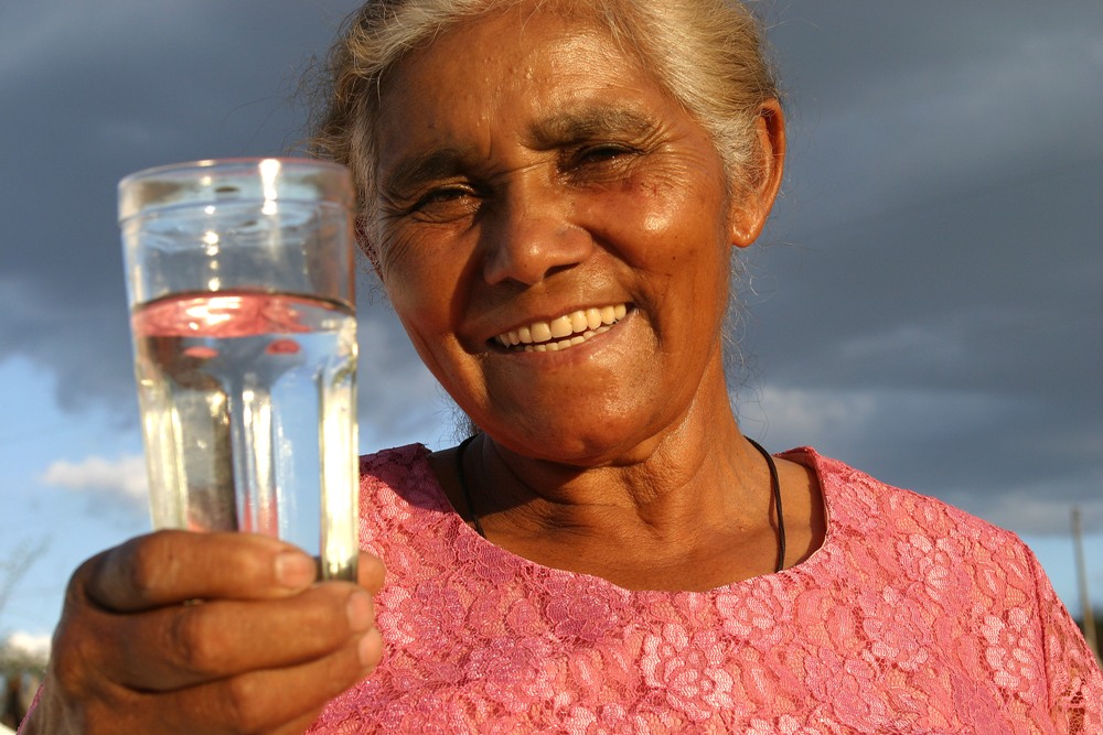 Mulher negra sorridente segurando copo de água