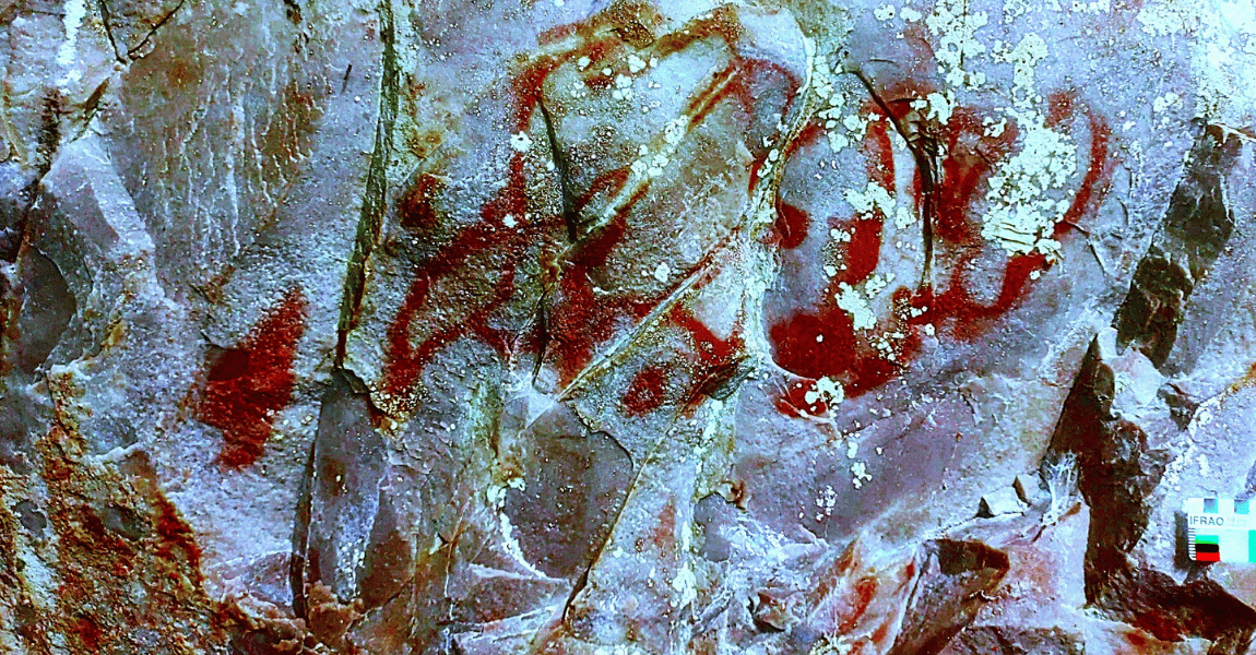 Imagem de uma parede de pedra com pinturas rupestres em tons vermelhos. Os traços parecem formas abstratas e símbolos antigos espalhados sobre a superfície rochosa clara e irregular.