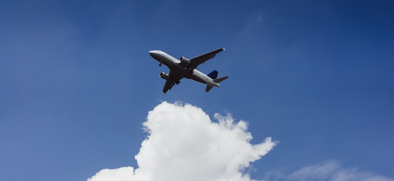 Avião de passageiros voando sobre um céu azul cheio de nuvens brancas.