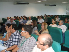 Imagem de auditório com várias pessoas sentadas nas cadeiras e olhando para frente.