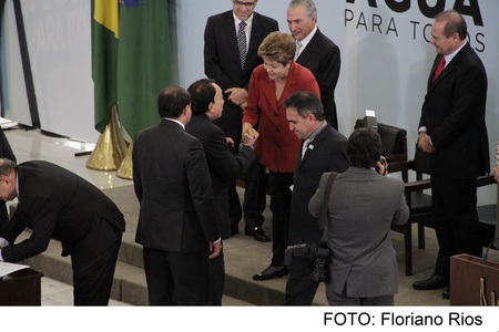 Imagem da presidente Dilma Rousseff, ao lado do vice Michel Temer, e outros membros do Governo Federal sorrindo e conversando entre si.