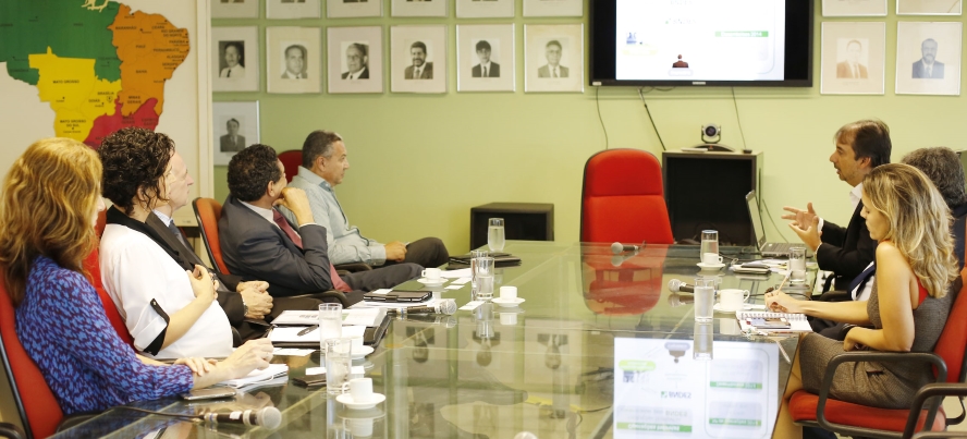 Foto de reunião entre corpo técnico da Sudene e representantes do BNDES. Todos estão conversando em uma sala de reuniões. Há uma apresentação em slides projetada em um telão.