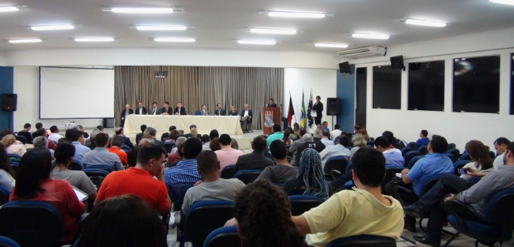 Foto de evento na Universidade Federal da Paraíba. Há pessoas sentadas numa plateia, outras em uma mesa em frente a elas e uma pessoa discursa em um púlpito.