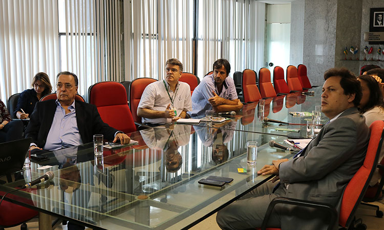 Participantes da reunião sentados à mesa, prestando atenção à apresentação.