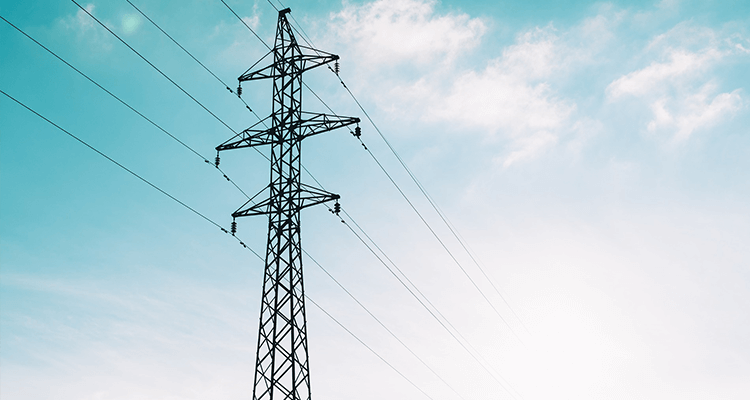 A foto mostra uma torre de transmissão de energia com um céu azul e nuvens ao fundo.