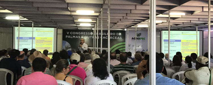 A foto mostra várias pessoas sentadas em cadeiras acompanhando uma palestra durante evento.