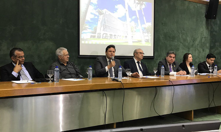 Superintendente Marcelo Neves sentado à mesa de abertura, falando ao microfone, ao lado de seis participantes