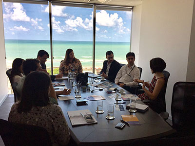 Participantes do encontro sentados a uma mesa, em uma sala de reunião da Apex-Brasil, em Recife