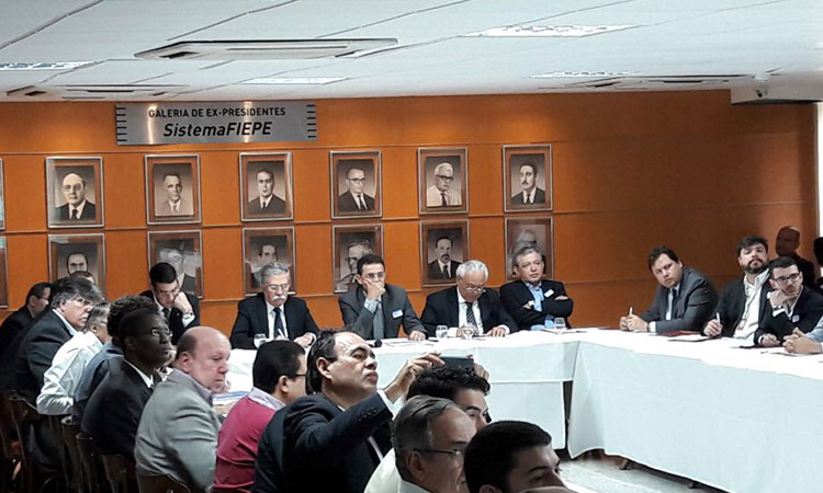 Participantes do encontro em uma mesa em formato de "U", tendo como fundo uma galeria de fotos dos ex-presidentes da FIEPE.