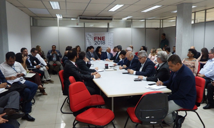 Mesa de reunião com quase todas as cadeiras ocupadas diversas disponibilizadas em "U" em volta mesa, todas ocupadas