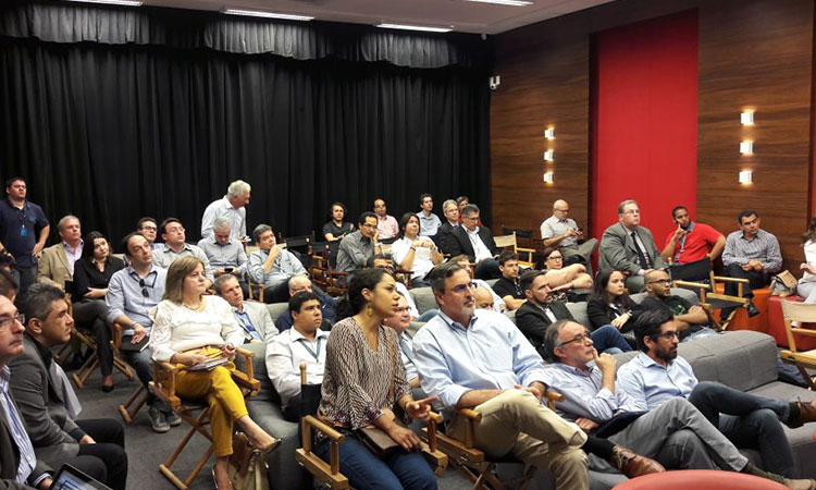 Foto da plateia assistindo às apresentações. Todos sentados.