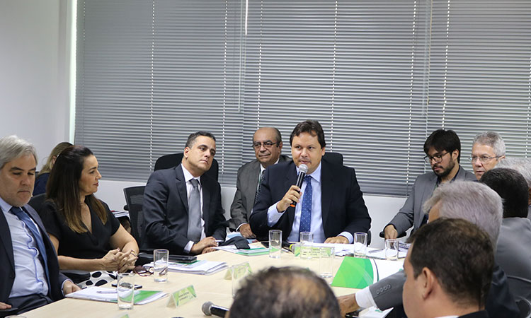 Mostra a mesa de reunião com alguns participantes.