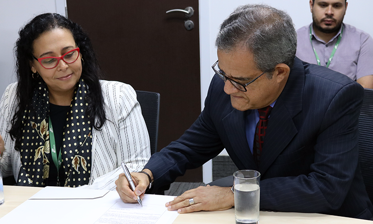 Novo diretor assinando Termo de Posse, ao lado da coordenadora de Gestão de Pessoas, Carla Paes.