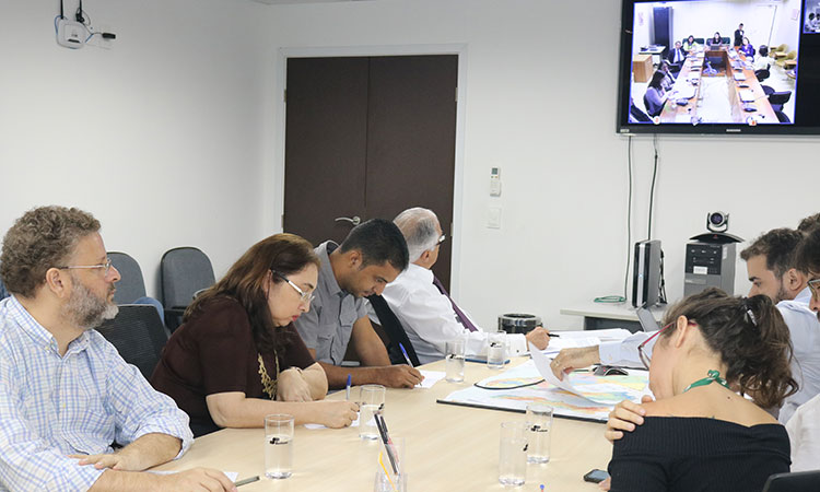 mesa de reunião com representantes da Sude e monitor com imagem dos outros participantes