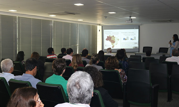 A foto mostra a plateia, o slide e a consultora da palestra sobre educação.