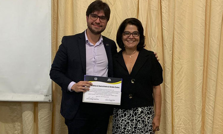 Rafael Feitosa segurando o diploma, ao lado da vice-reitora