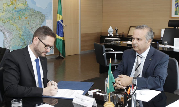 Superintendente e ministro sentados a mesa durante solenidade de posse. Evaldo está assinando o documento.